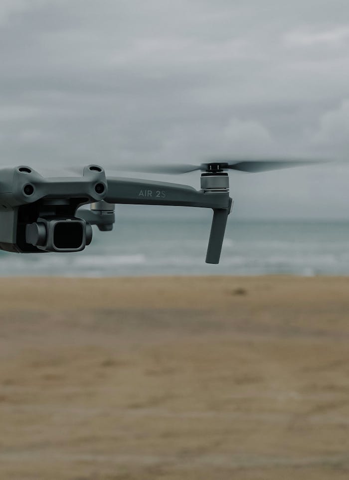 Mastering the First Impression: Your intriguing post title goes here Gray drone captured in mid-flight over a beach under a cloudy sky, showcasing modern aerial technology.