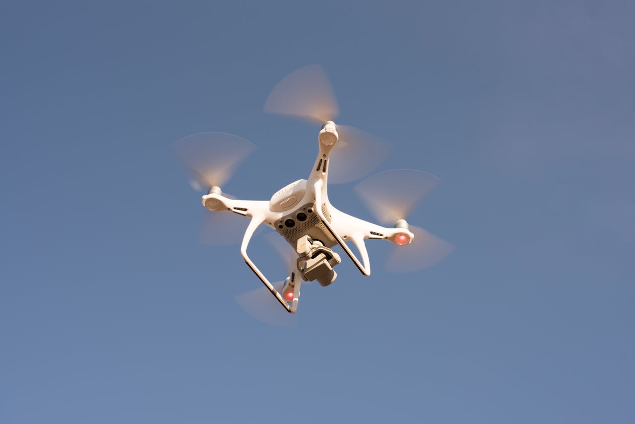 A white drone in flight against a clear blue sky, capturing aerial footage with precision.